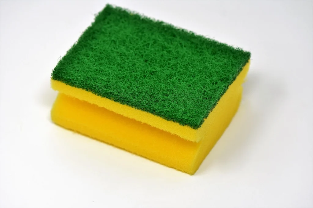 Yellow and green household cleaning sponge used for scrubbing and washing dishes on a white background.