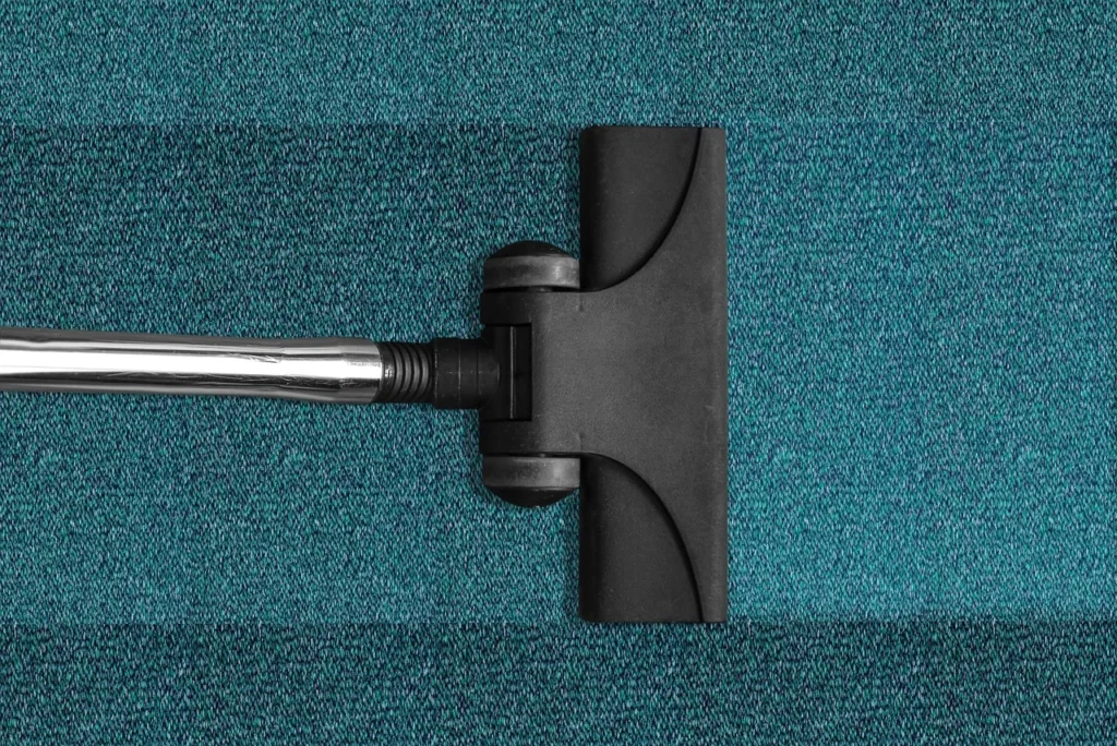 Black vacuum cleaner head cleaning a teal carpet with a metal handle visible from above.